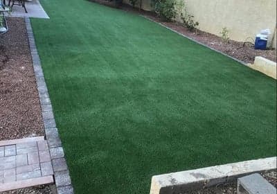 Lush green artificial grass lawn with stone edging in a residential backyard setting.