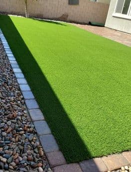 Lush green artificial grass yard with stone border and sunlight shadowing the lawn.