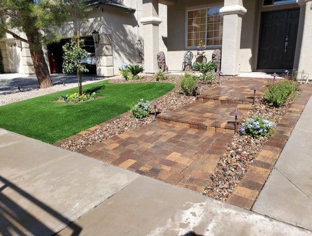 Landscaped front yard with stone pathways, artificial grass, and decorative plants.