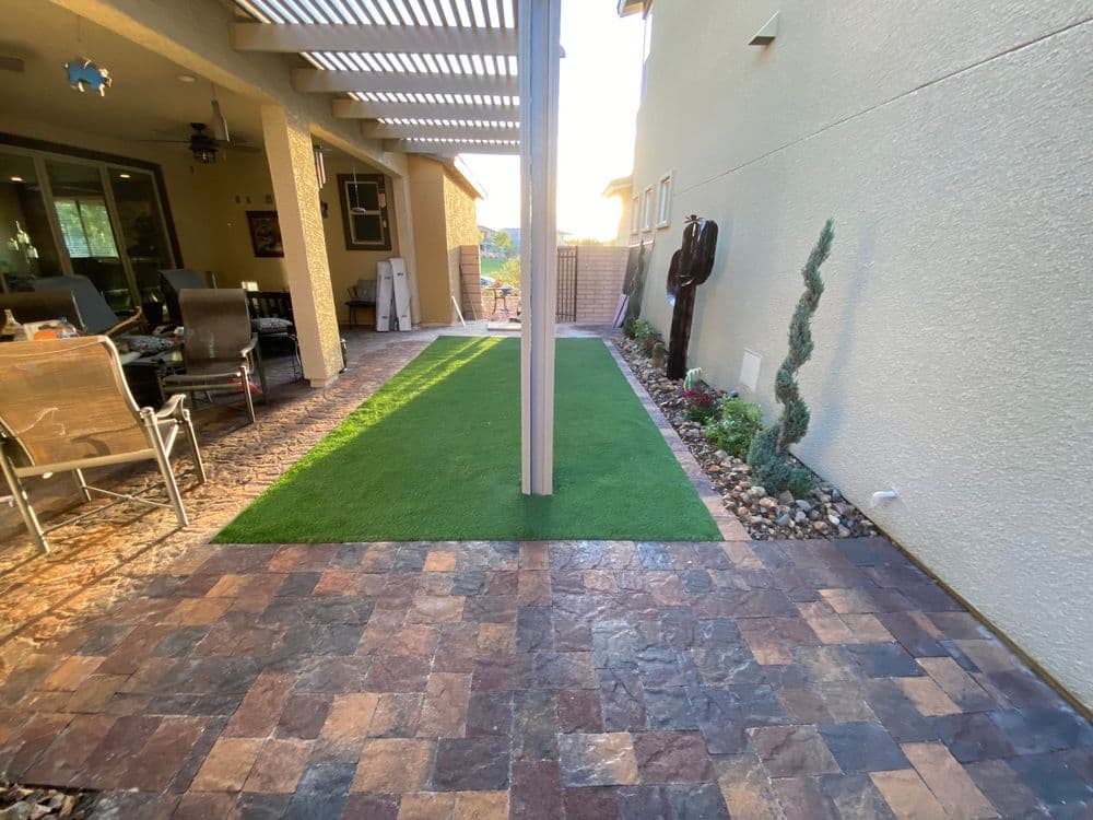 Lush green lawn separates paved patio in a sunlit backyard with landscaping.